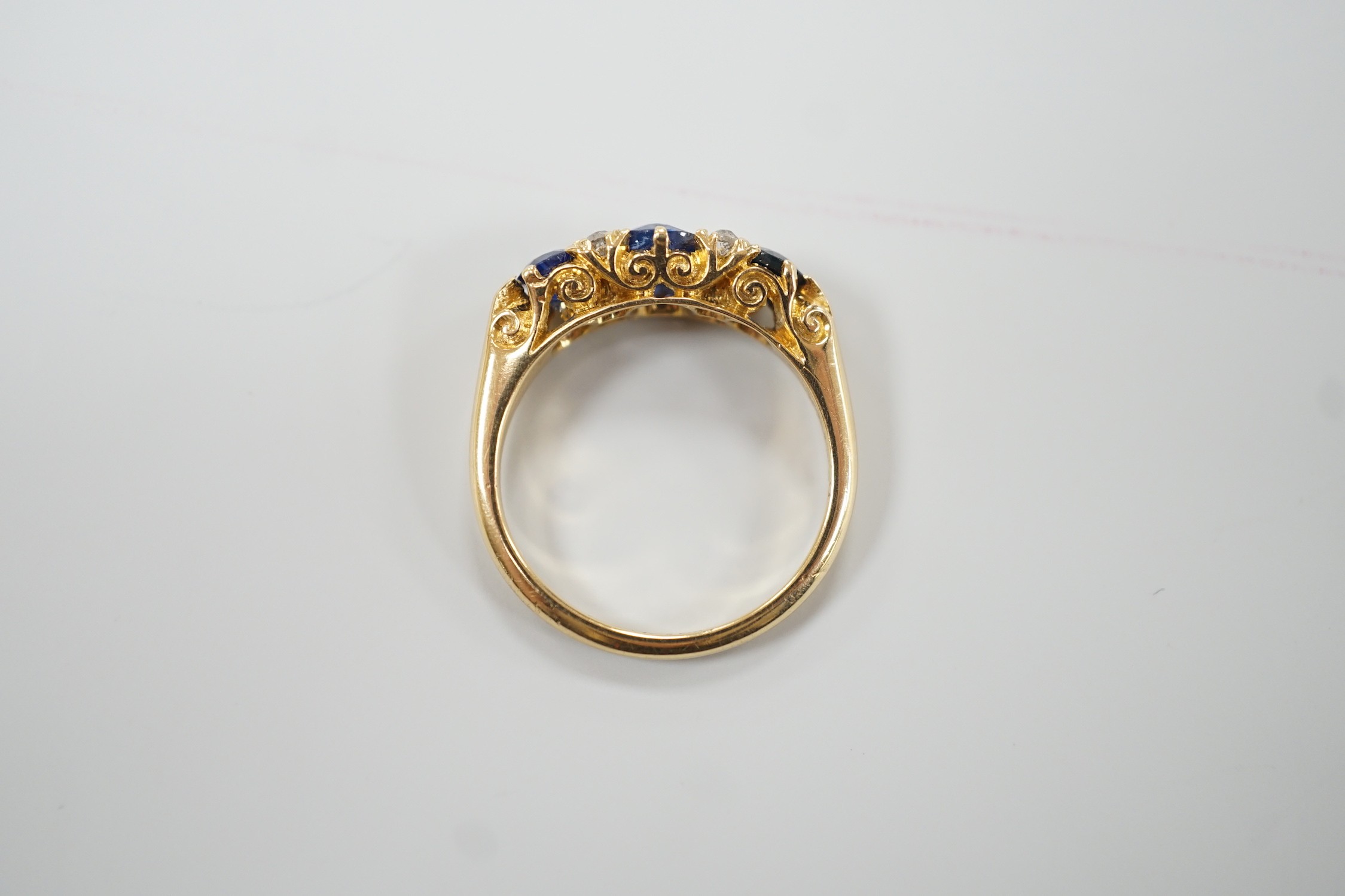 A George V 18ct gold and three stone sapphire set half hoop ring, with four diamond chip spacers, size M, gross weight 4.4 grams.